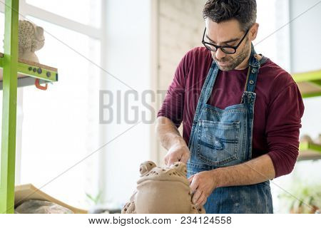 Ceramist Dressed in an Apron Sculpting Statue from Raw Clay in the Bright Ceramic Workshop.
