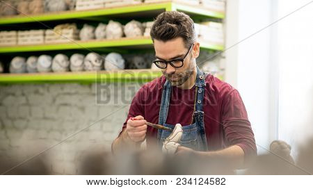 Portrait of Ceramist Dressed in an Apron Working on Clay Sculpture in the Bright Ceramic Workshop.