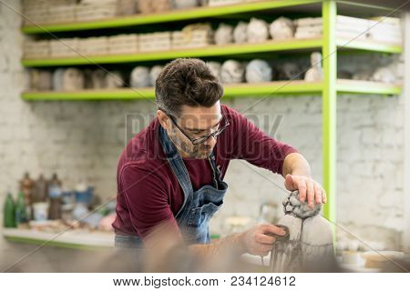 Portrait of Ceramist Dressed in an Apron Working on Clay Sculpture in the Bright Ceramic Workshop.