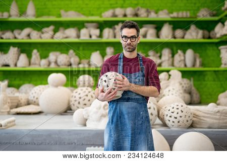 Portrait of Young Ceramist in the Bright Modern Ceramic Workshop Holding his Sculpture. Small Business Concept.