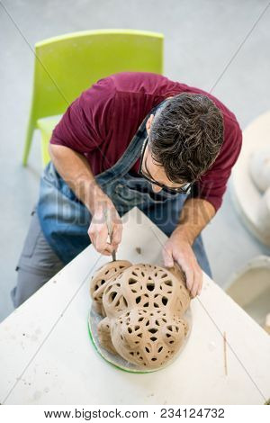 Topview of Ceramist Dressed in an Apron Sculpting Statue from Raw Clay in the Bright Ceramic Workshop.