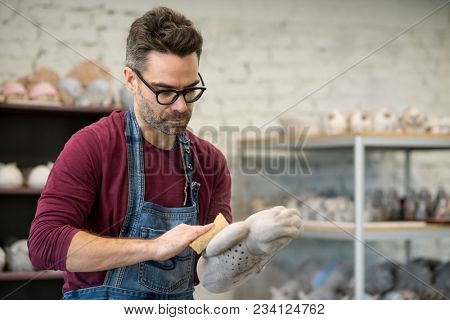 Portrait of Ceramist Dressed in an Apron Working on Clay Sculpture in the Bright Ceramic Workshop.