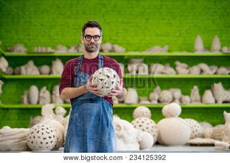 Portrait of Young SmilingCeramist in the Bright Modern Ceramic Workshop Holding his Sculpture. Small Business Concept.