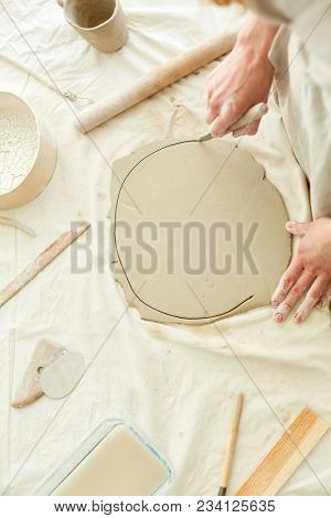 Creative handcraftswoman cutting circle from flat piece of clay with special handtool on table
