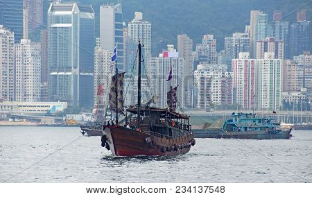 A Typical Chinese Ship, Junk, In Kowloon Bay Against The Skyscrapers Of Hong Kong