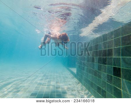 A Child Boy Is Swimming Underwater In A Pool, Smiling And Holding Breath, With Swimming Glasses.