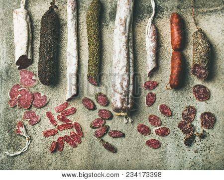 Variety Of Spanish Or Italian Cured Meat Sausages. Flat-lay Of Fuets And Salamies Cut In Slices Over