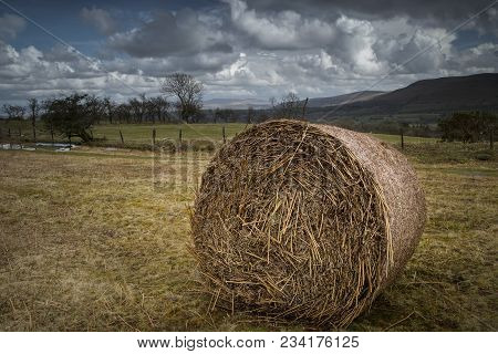 A Rural Landscape Scenic View, With Overcast Sky, Mountains, Hills And Large Haystack In Foregound