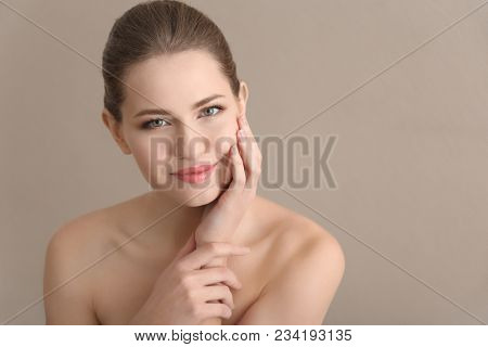 Young woman applying cream onto her skin against color background