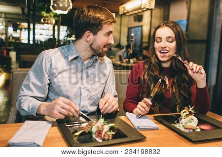 Man And Woman Are Eating At The Table In Restaurant And Talking To Each Other. They Are Enjoying Com