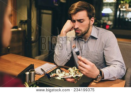 Pictue Of Guy Sitting Together With His Girlfriend And Eating Some Food They Have Ordered. Man Has F