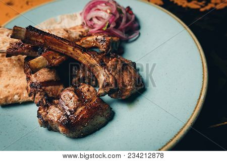 Rosemary Seasoned Lamb Rack, Ribs With Rice Garnish On A Black Plate Close Up Side View.luxury