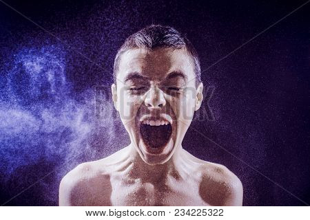 Pre Teen Boy Angrily Screams Into A Spray Of Water Against A Black Background. Toned Image.