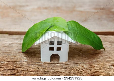 Miniature White Toy Model House With Green Leaves On Wooden Backgdrop. Eco Village, Abstract Environ