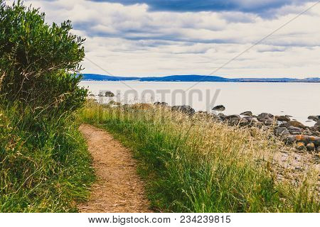 Deserted Beach In Hobart, Tasmania With Rocks And Walkpath In The Foreground On An Overcast Day With