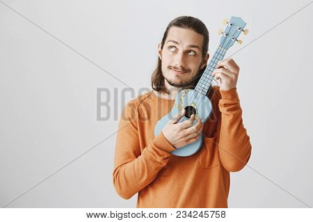 Tuning Strings To Show Amazing Playing Skill. Portrait Of Handsome Funny Musician In Orange Sweater 