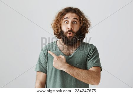 Shock Content Behind This Corner. Indoor Shot Of Amazed And Stunned Eastern Male With Beard And Curl