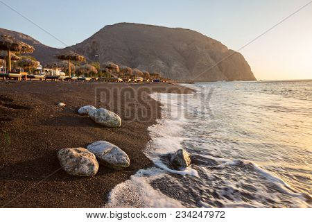 Perissa beach during sunrise on the Greek island of Santorini with sunbeds and umbrellas.