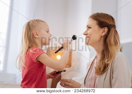 Mother And Daughter. Pleasant Nice Cheerful Girl Holding A Brush And Looking At Her Mother While Doi