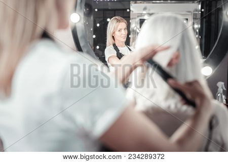 Professional Hairdresser. Nice Smart Professional Woman Looking Into The Mirror And Combing Hair Of 