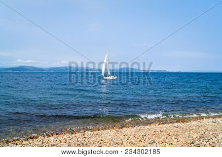 A Sailboat Is A Yacht With White Sails. A Ship In The Picturesque Bay Of Putyatin Island In The Far 