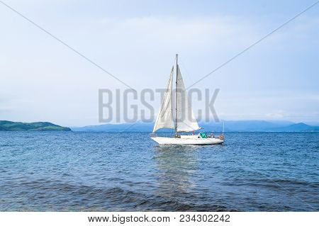 A Sailboat Is A Yacht With White Sails. A Ship In The Picturesque Bay Of Putyatin Island In The Far 
