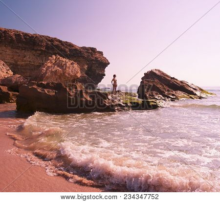 A Girl Stands On The Rocky Shore Of The Ocean And Looks Into The Distance, Oman.