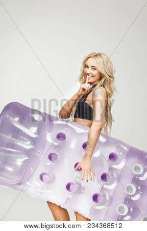 Beautiful Blond Woman In Swimsuit Holds An Air Mattress On White Isolated At Hand, Applies A Finger 