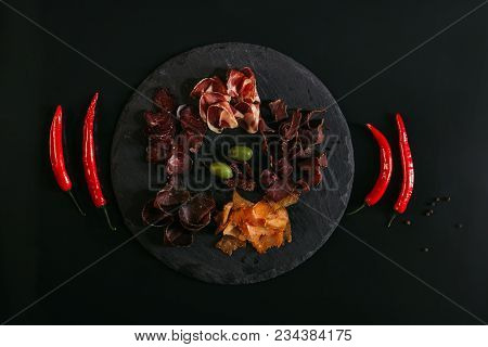 Top View Of Gourmet Assorted Meat With Olives On Slate Board And Chili Peppers On Black