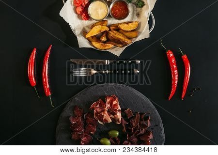 Top View Of Baked Potatoes With Sauces, Chili Peppers, Fork, Knife And Gourmet Assorted Meat On Slat