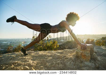 athletic young african american woman doing stretches and pushups at runyon canyon with view of los angeles in background