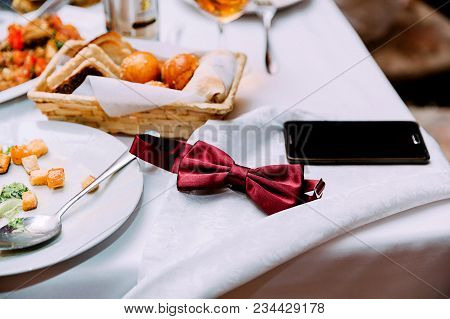 Bow Tie And Phone Carelessly Lie On A Festive Table Amid A Meal