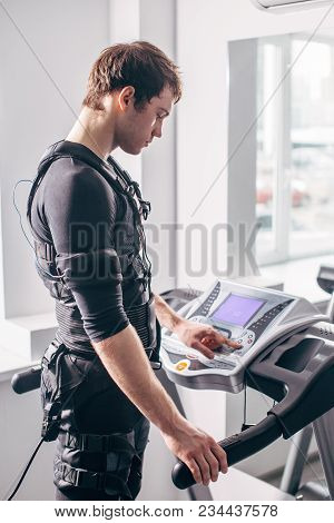 Ems Training. Fit Man Wearing Black Electromiostimulation Suit Preparing For Running On Treadmill Ne