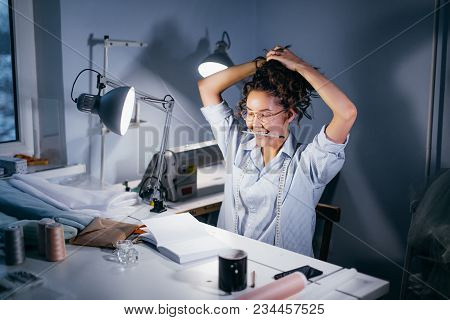 Seamstress Wearing Glasses With Pencil On Arms Collecting Her Hair At The Light Table