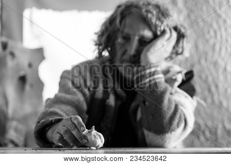 Monochrome Image Of Concerned Man With Long Hair And A Sweater Full Of Holes Sitting At A Table Indo