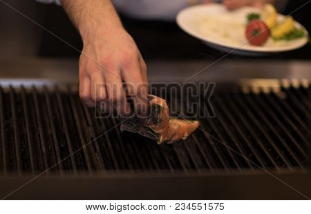 Master chef hands cooking grilled salmon fish with potatoes on a restaurant kitchen