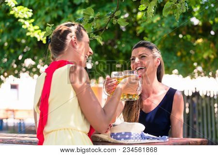 Women in beergarden having refreshment sitting under tree in the shade as it is hot