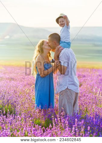 Mom, Dad And Their Little Son Are Walking In A Lavender Field. Life In Provence. Kissing Parents