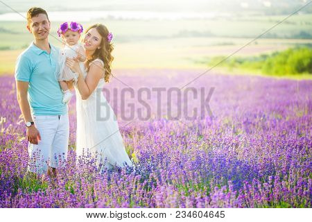 Mom, Dad And Their Little Daughter In A Beautiful Wreath Are Walking In A Lavender Field. Life In Pr
