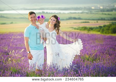Mom, Dad And Their Little Daughter In A Beautiful Wreath Are Walking In A Lavender Field. Life In Pr