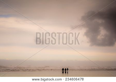 Group Of People Walking On A Sandy Beach In Wet Weather