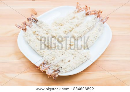 Close-up Of Raw Tempura Shrimps In A Breaded Lay On A White Plate That Stands On A Wooden Table. Mar