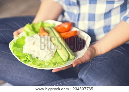 A Girl Holds A Plate With Rice And Vegetables. Healthy Eating Concept. Girl In Jeans And A Plaid Shi