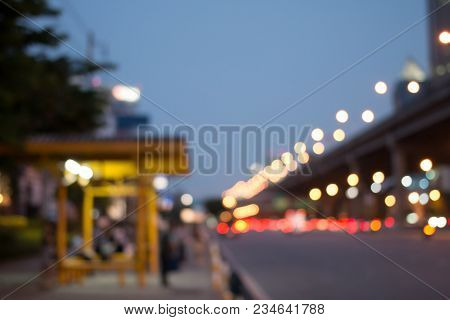 Blurred Image Of Passengers Wating For Bus With A City Street At Bus Station In Night Time, A Public
