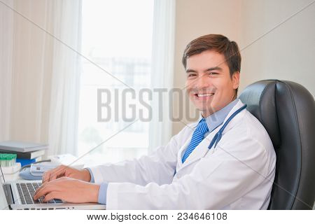 Smiling Doctor Posing In The Office, He Is Wearing A Stethoscope, Medical Staff On The Hospital Back