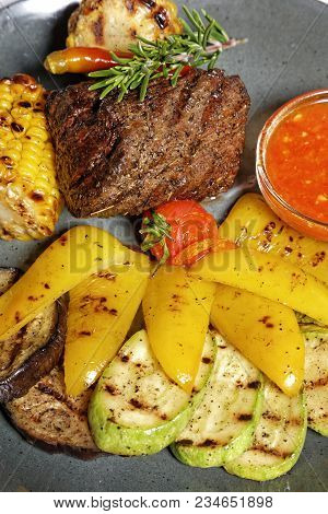Fried Meat With Garnish Of Pepper, Zucchini, Tomato And Corn With Ajika Sauce Served On A Gray Plate