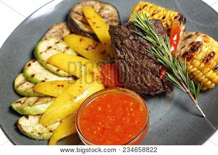 Fried Meat With Garnish Of Pepper, Zucchini, Tomato And Corn With Ajika Sauce Served On A Gray Plate