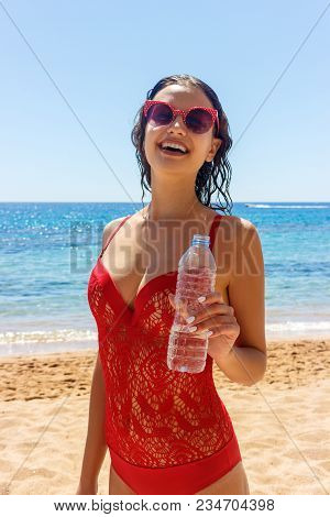 Happy Tanned Girl Holding A Water Bottle On The Beach.