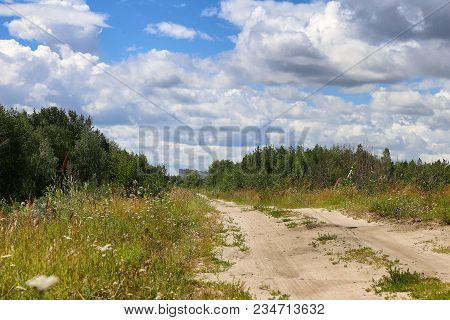 Rural Road And The Blue Sky. The Road Leaves Afar. Grass, White Cloud And Green Trees.