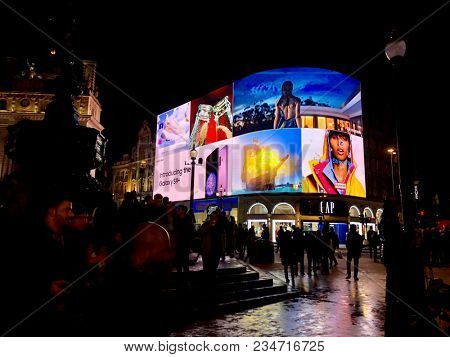 LONDON - APRIL 4, 2018: Tourists lit up at night by bright advertising illumination screens in Piccadilly Circus, Westminster, London, UK.
